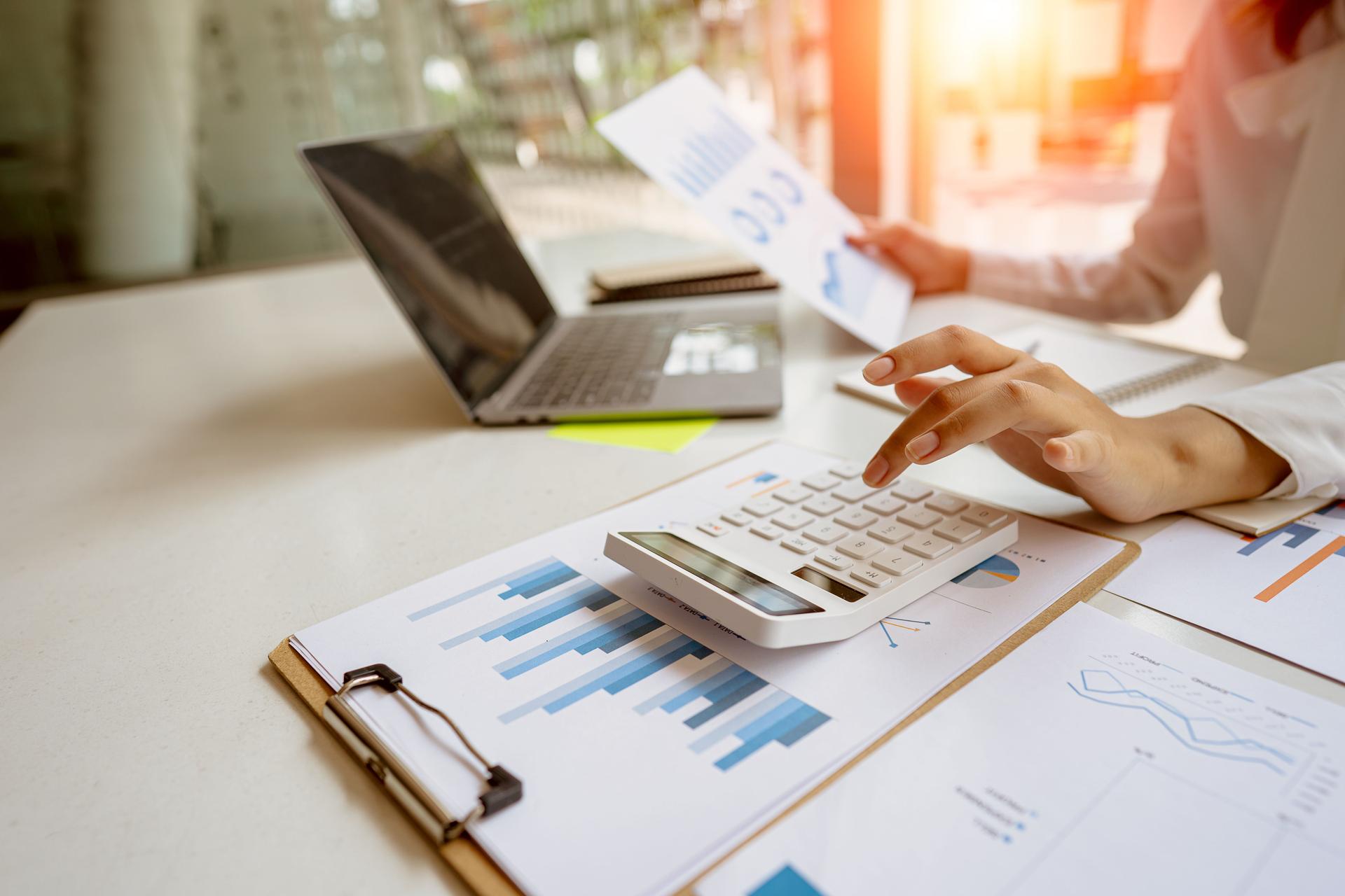 A businessman presses a white calculator to calculate numbers in company financial documents. The finance department prepares accounting documents, analyzing income and expenses in the business.