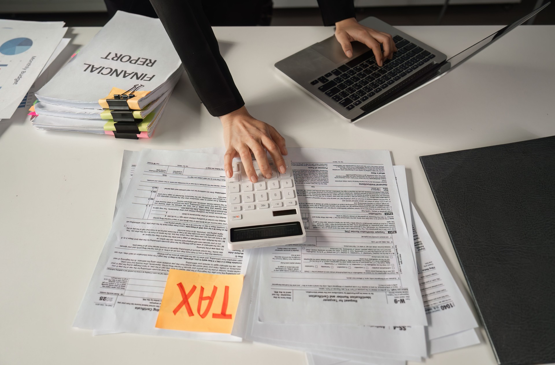Businesswoman calculating finances using a calculator and managing tax paperwork.